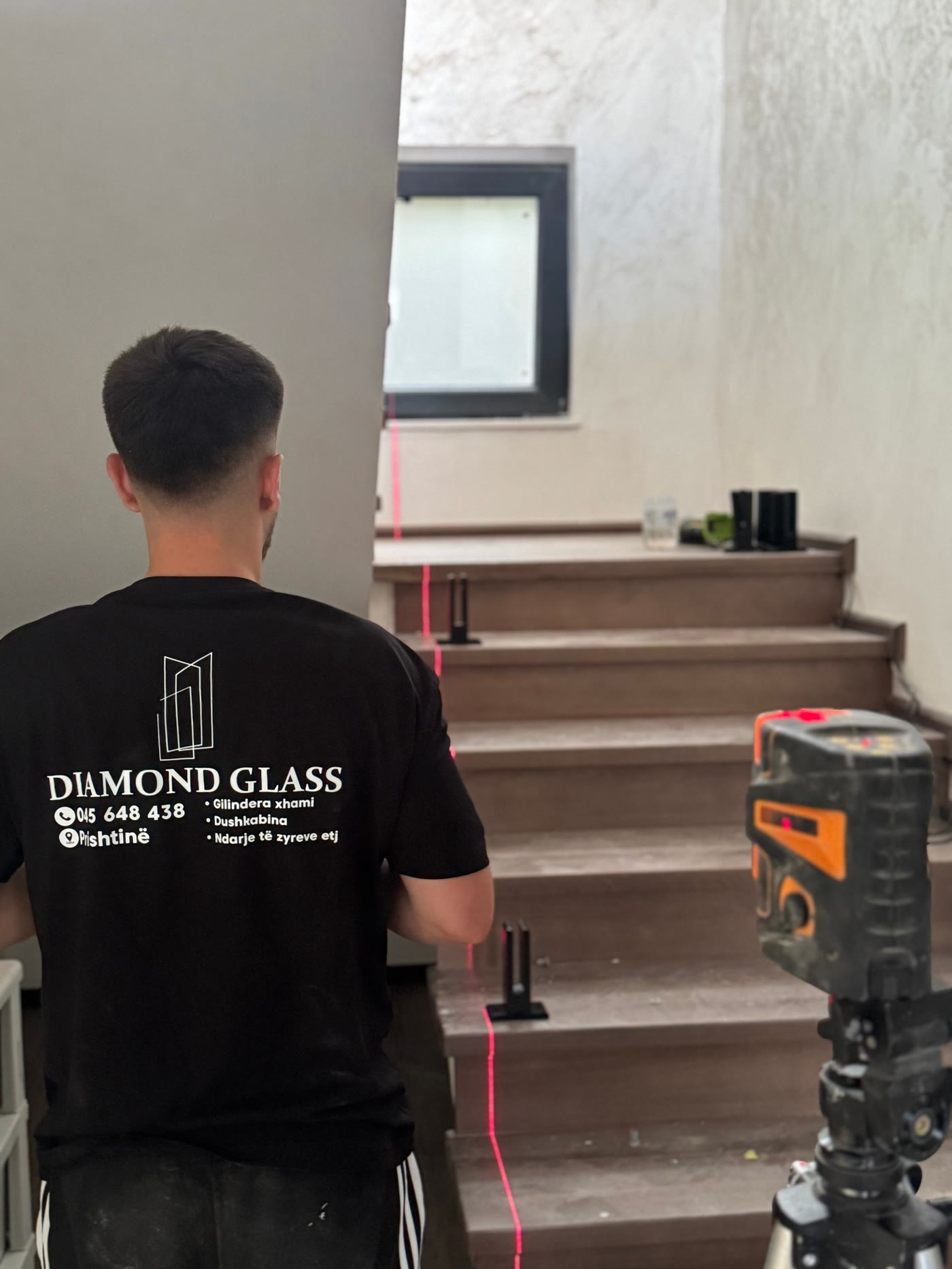 Punëtor i Diamond Glass me bluzë të markës gjatë montimit të një parmaku qelqi